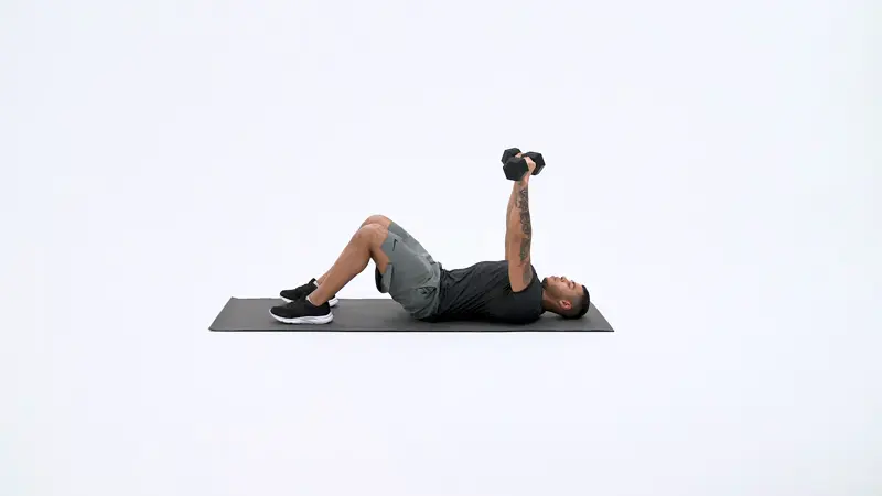 A man is performing floor dumbbell press on a fitness mat, lateral head tricep exercises