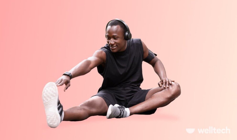 a man in black sportswear and headphones is stretching his leg, smiling, leg day warm-up
