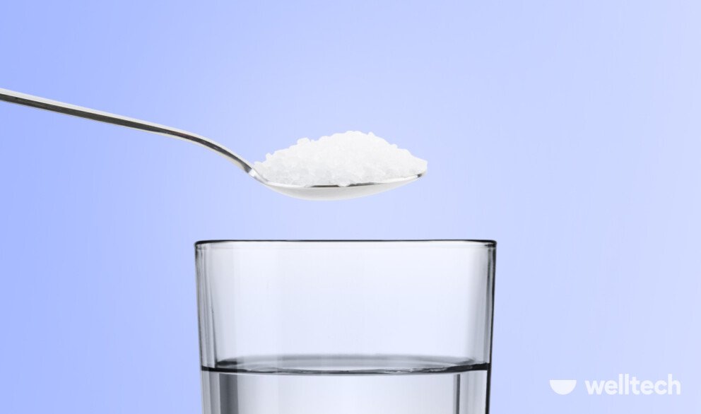 a glass of water with a teaspoon with salt on top of it, drinking salt water benefits