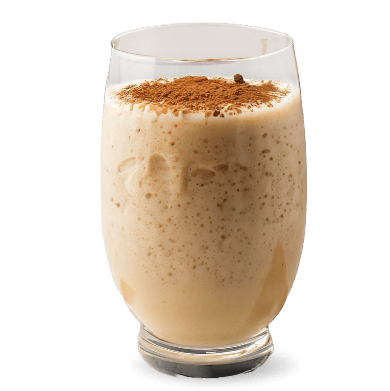 a creamy and frothy smoothie named Nutty Banana Crunch in a clear glass. The smoothie has a light beige color, indicative of banana as a primary ingredient, with a sprinkle of brown topping that could be ground nuts or a spice like cinnamon or nutmeg, providing the 'crunch' aspect in the name. The texture of the smoothie appears thick and rich, with visible bubbles on the surface suggesting a freshly blended beverage
