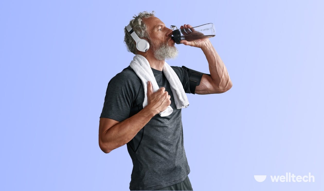 a man is drinking water while during workout, wearing headphones and a towel on his neck